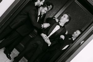 Black and white photo of four men in formal tuxedos socializing at an elegant event.