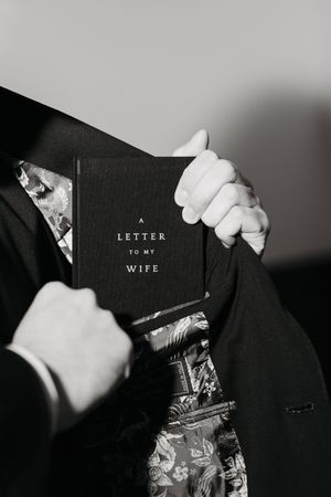 Groom placing a letter to my wife journal into his suit pocket on wedding day, black and white photo.