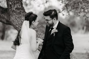 Black and white wedding photo of bride and groom sharing a tender moment under a tree.