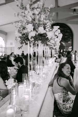 Black and white photo of a wedding reception with tall floral centerpieces and candles on a long elegant table.