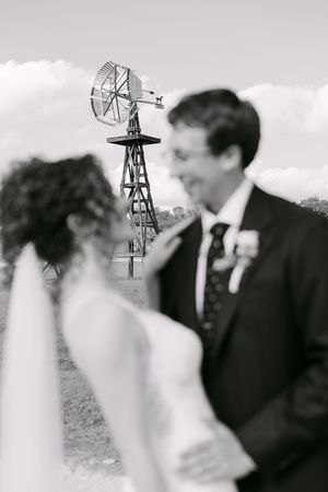 Black and white photo of a bride and groom sharing a romantic moment with a windmill in the background.