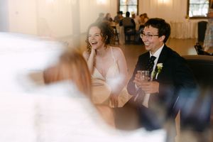 Bride and groom laughing joyfully during wedding reception speeches in an elegant venue.
