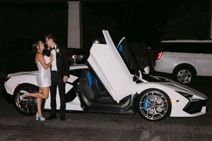 Couple kissing beside a white Lamborghini with scissor doors open at night.