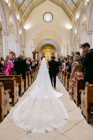 Bride walks down the aisle in a stunning cathedral-length veil in an elegant white church wedding ceremony.