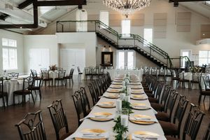 Elegant wedding reception hall with long dining tables, gold place settings, grand staircase, and crystal chandelier.