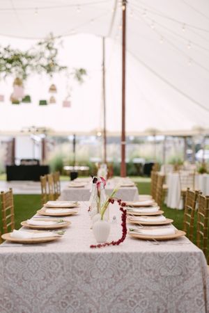 Elegant outdoor wedding reception table set under a white tent with gold chiavari chairs, damask linens, and floral centerpieces.