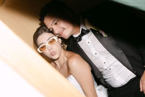 Couple posing playfully at wedding, woman in white dress with sunglasses, man in black tuxedo, candid photo booth style.