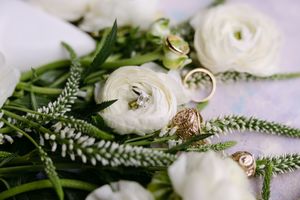 White ranunculus bouquet with gold wedding rings nestled among green foliage on a soft background.