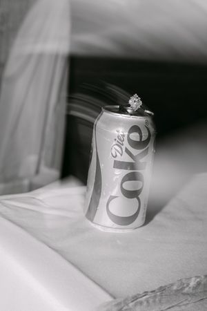 Black and white photo of a diamond engagement ring resting on top of a Diet Coke can with a wedding veil backdrop.