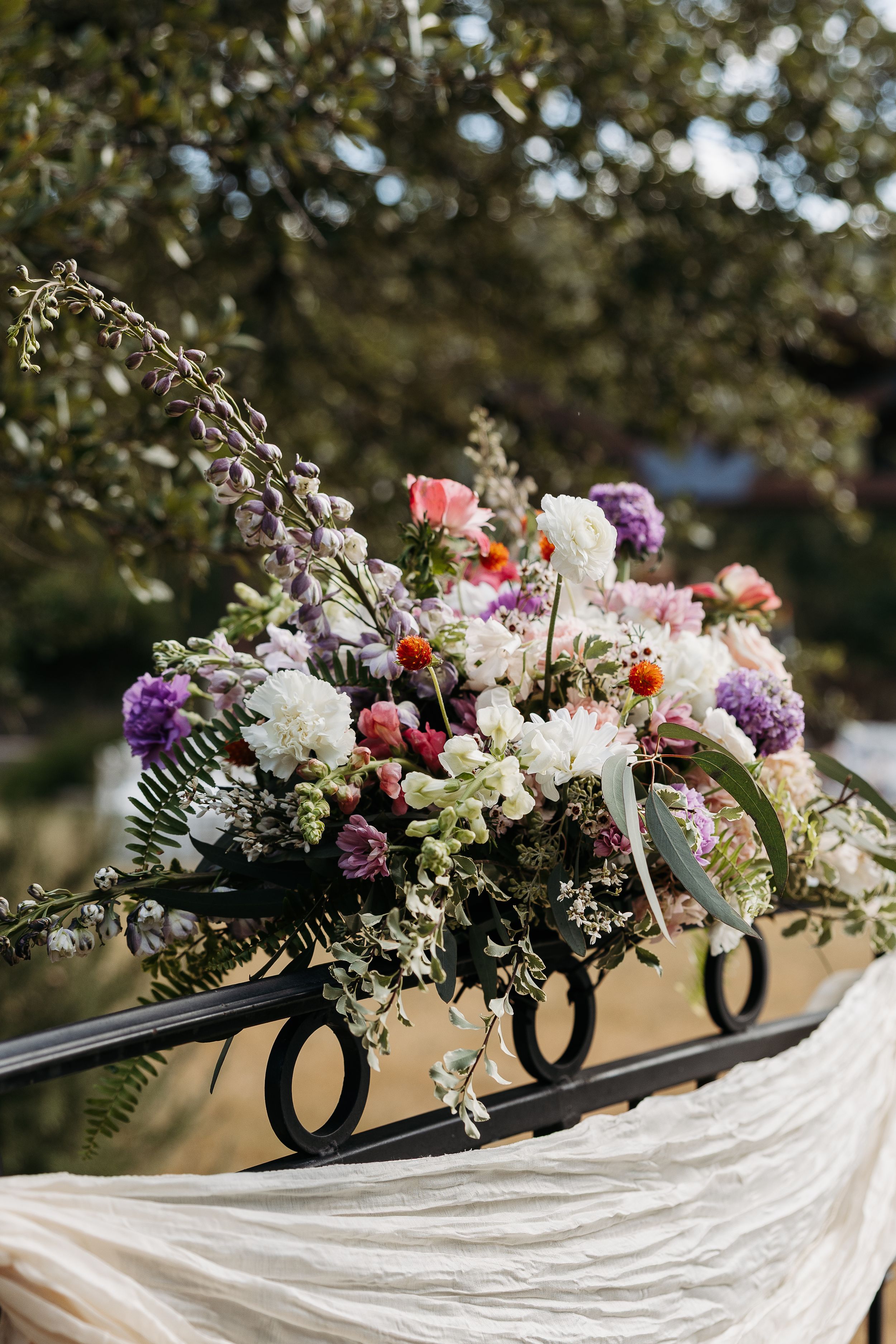 Elegant floral centerpiece with purple, pink and white flowers arranged in black letters on flowing white fabric.