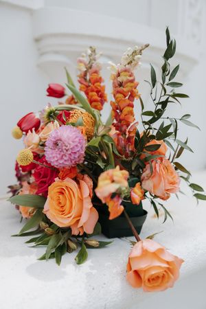 A series of floral arrangements featuring peach roses, pink dahlias, and orange blooms with greenery on a white surface.