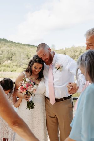 Wedding party shares joyful laughter together outdoors with desert mountains in background.