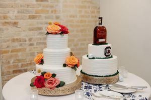 White wedding cake decorated with orange roses and black ribbon sits on display at elegant reception venue.