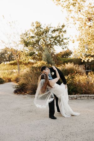 A romantic wedding couple performs a dramatic dip pose during sunset in an outdoor desert setting.