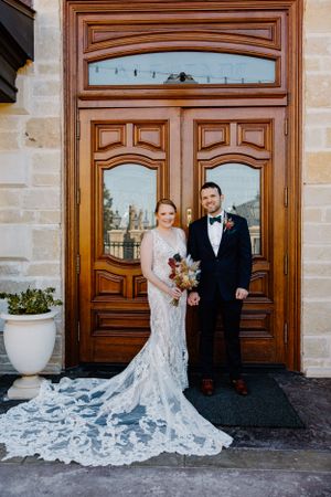 Couple poses in front of elegant wooden doors showcasing bride's dramatic lace train.