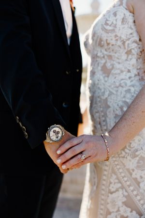 Close-up of wedding couple's hands with rings against formal attire.