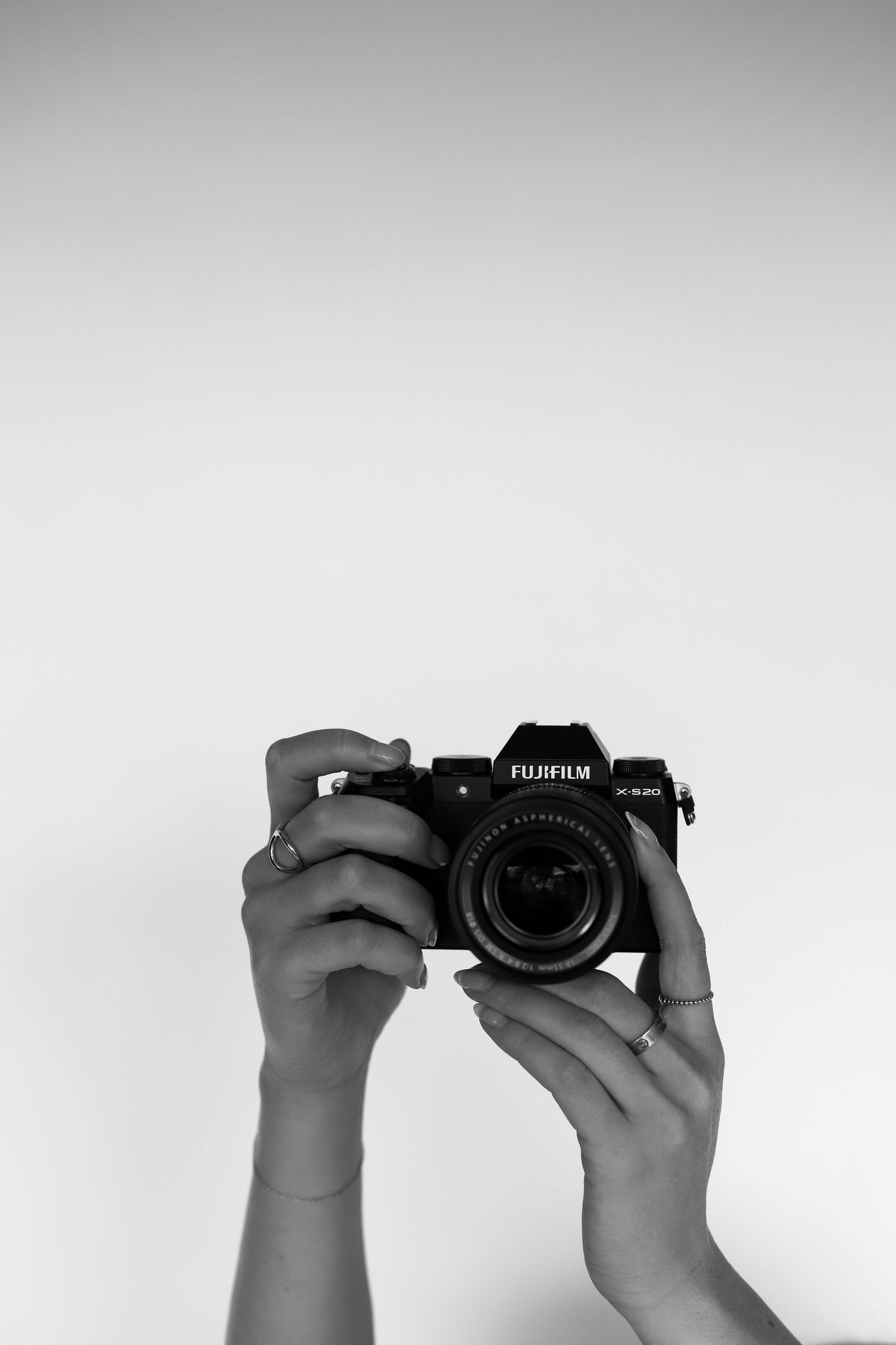 Hands demonstrating different angles of holding a Fujifilm camera against a white background.