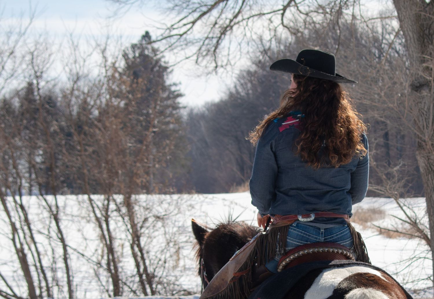 Cowgirl riding away on her horse, looking to the side in a Wisconsin winter scene