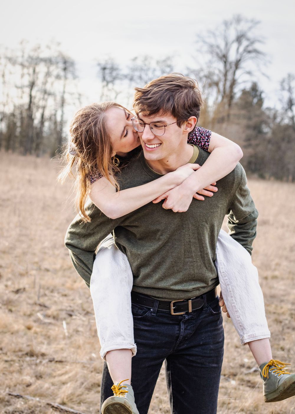 a woman is carried on the back of a man, they smile at each other as they walk through a golden field