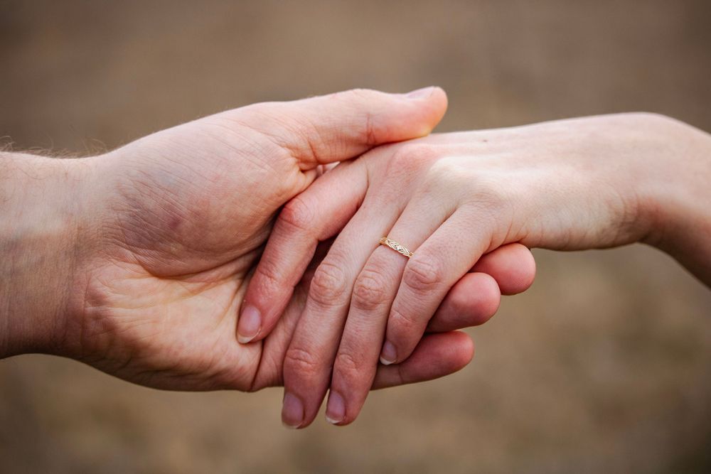 close up of a couple's hands, showing off the engagement ring with a blurred background