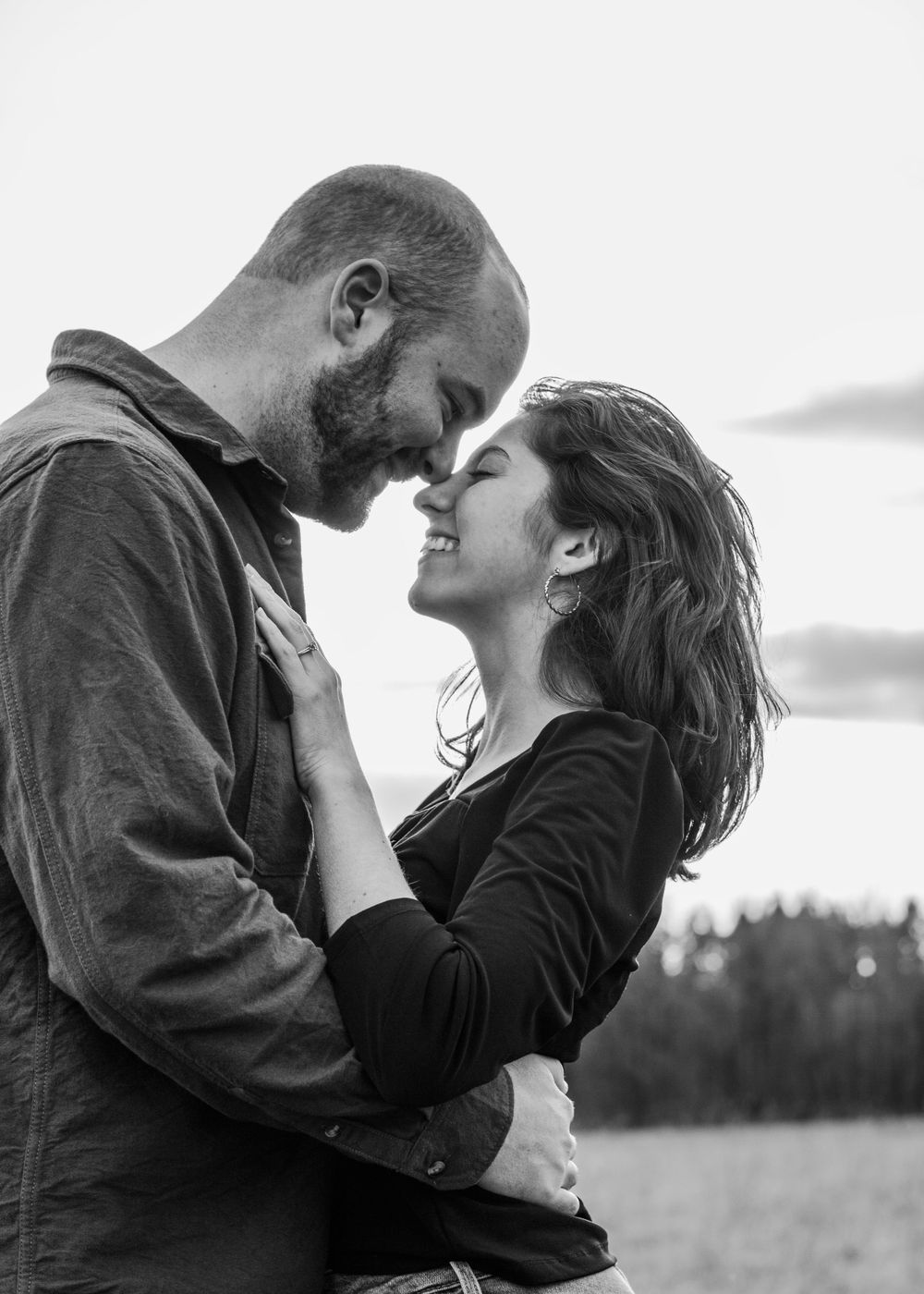 black and white image of a couple silhouetted against the sky. their faces are close and they smile at each other