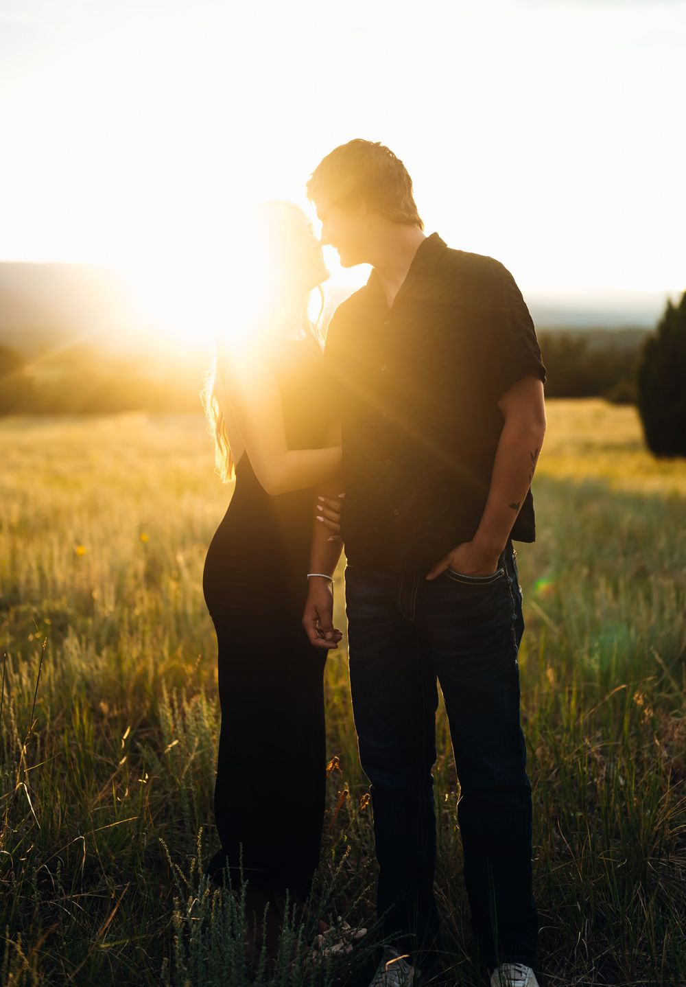 Two silhouettes stand together in a sunlit field during golden hour.