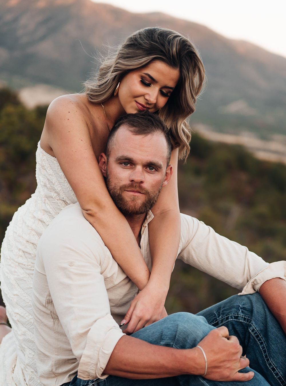 A romantic couple embraces outdoors with mountains in background during golden hour. Intimate candid engagement session in Colorado