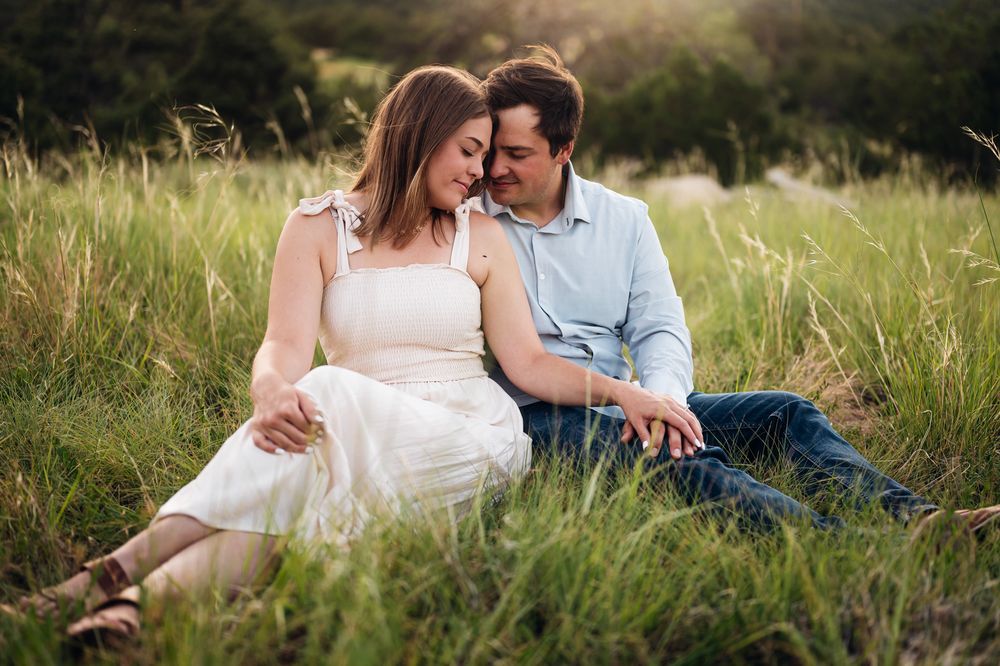 Couple sitting together in tall grass during golden hour sunset sharing an intimate moment in nature.