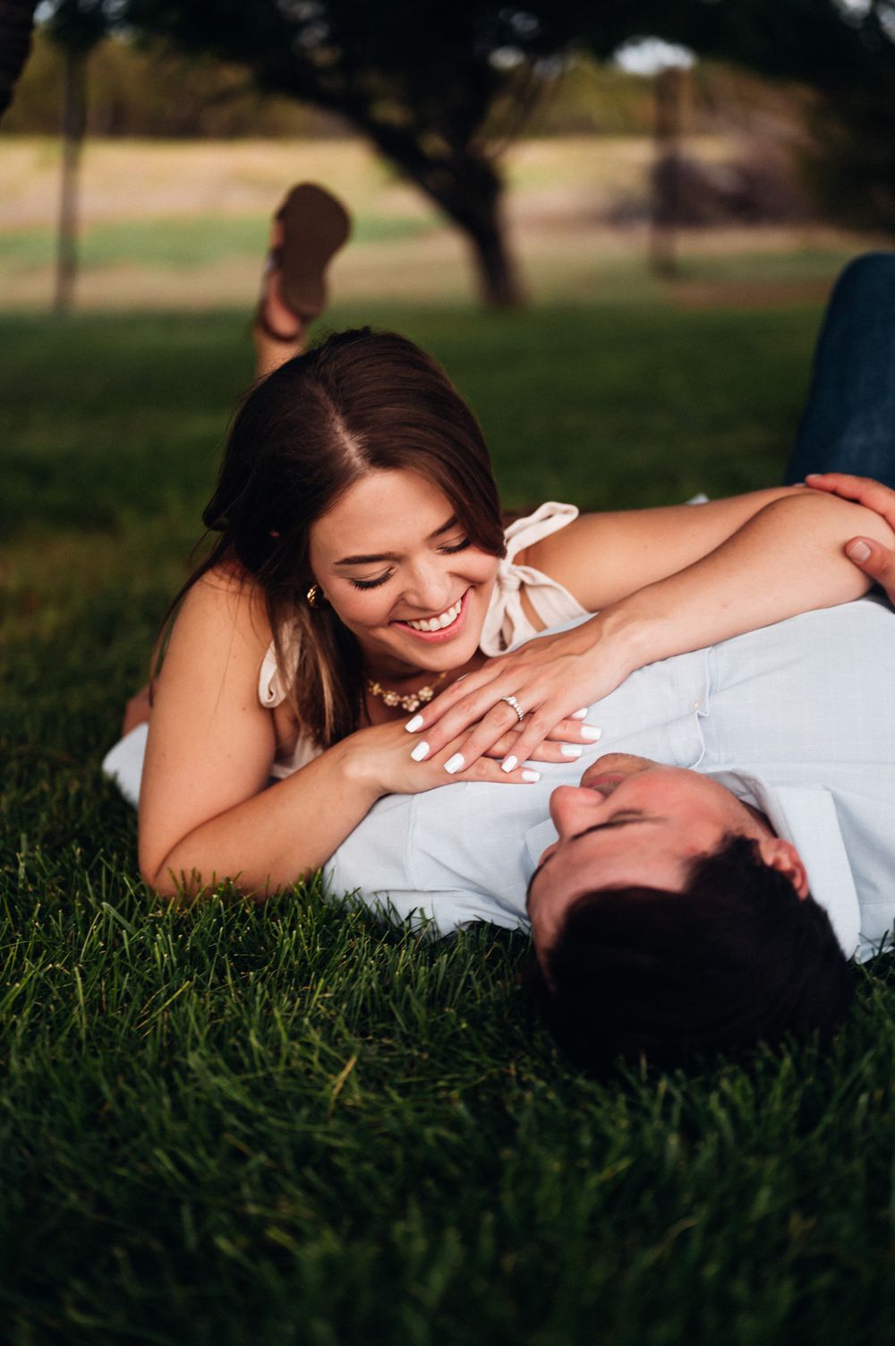 Couple laying in green grass outdoors sharing an intimate moment together in warm sunlight.