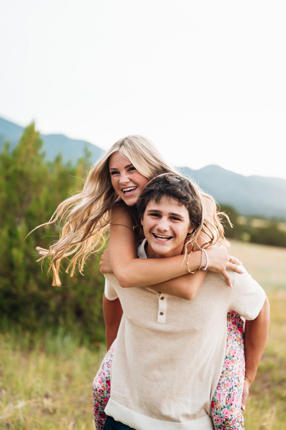 A couple shares a joyful piggyback moment together in a scenic mountain field during sunset.