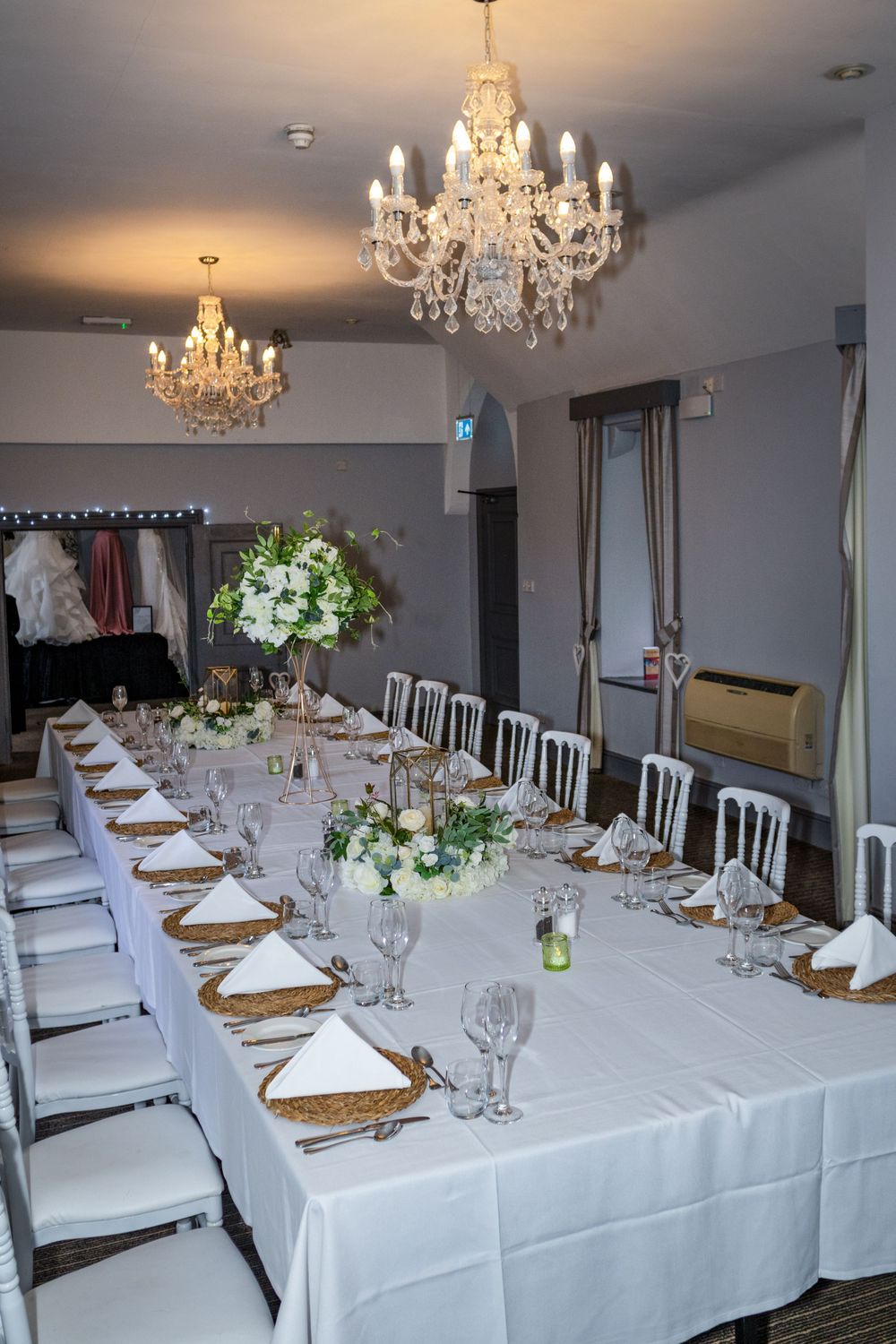 Long formal dining table with crystal chandeliers and white floral centerpieces.