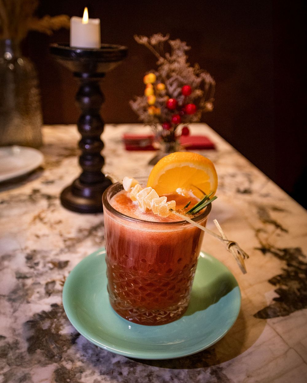 Festive cocktail with orange garnish served in a crystal glass on turquoise saucer with candlelight ambiance.