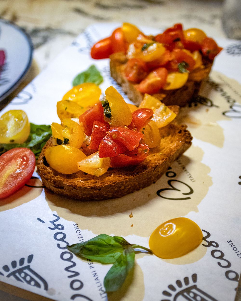 Colorful bruschetta topped with yellow and red cherry tomatoes and fresh basil leaves served on a patterned paper.