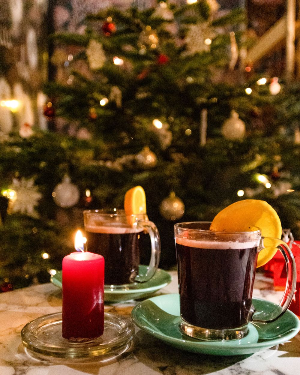 Two mugs of mulled wine with orange slices against a decorated Christmas tree background.