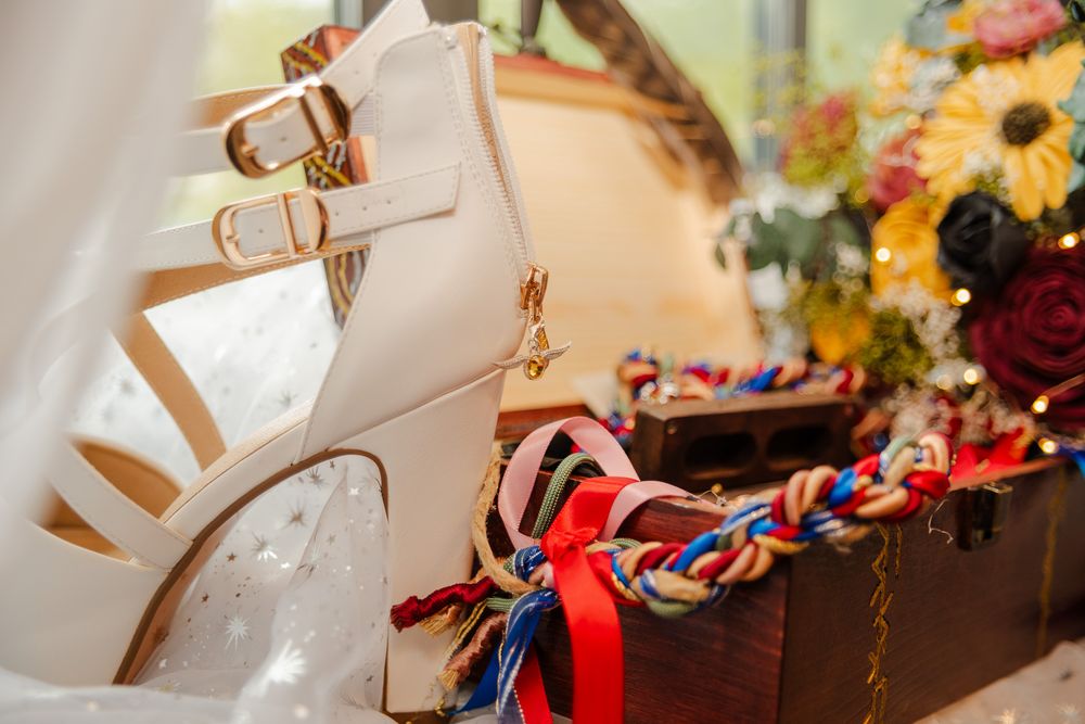 White strappy bridal heels displayed on wooden chest with colorful braided cord decorations.