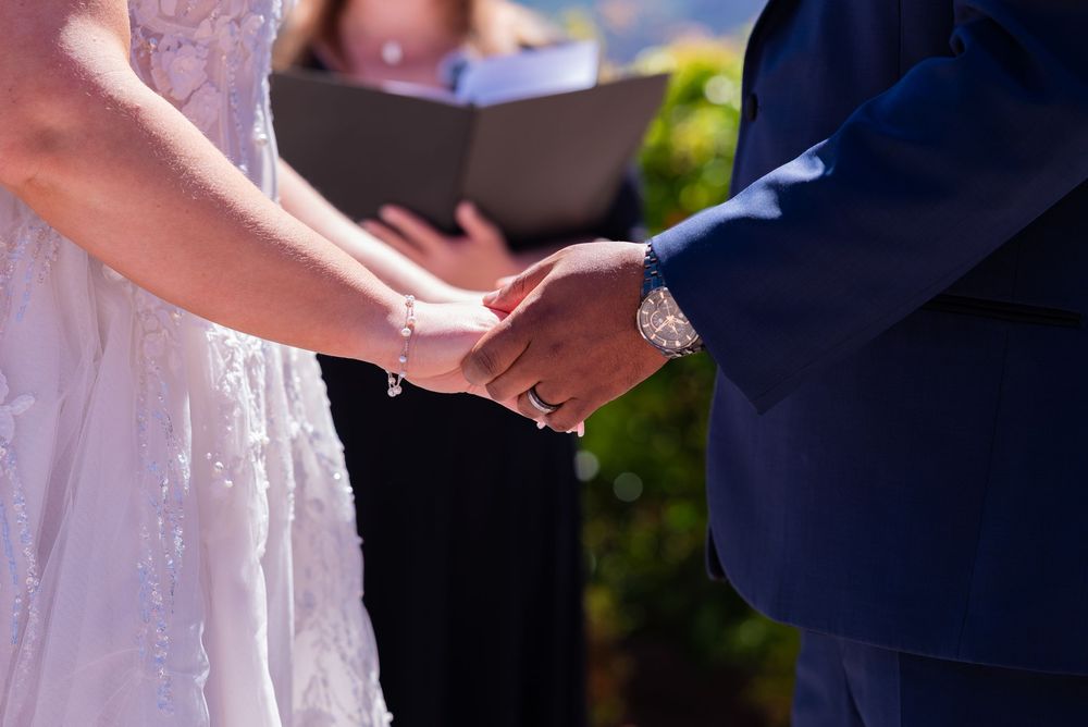 Bride and groom exchange rings during outdoor wedding ceremony, close-up of hands holding.