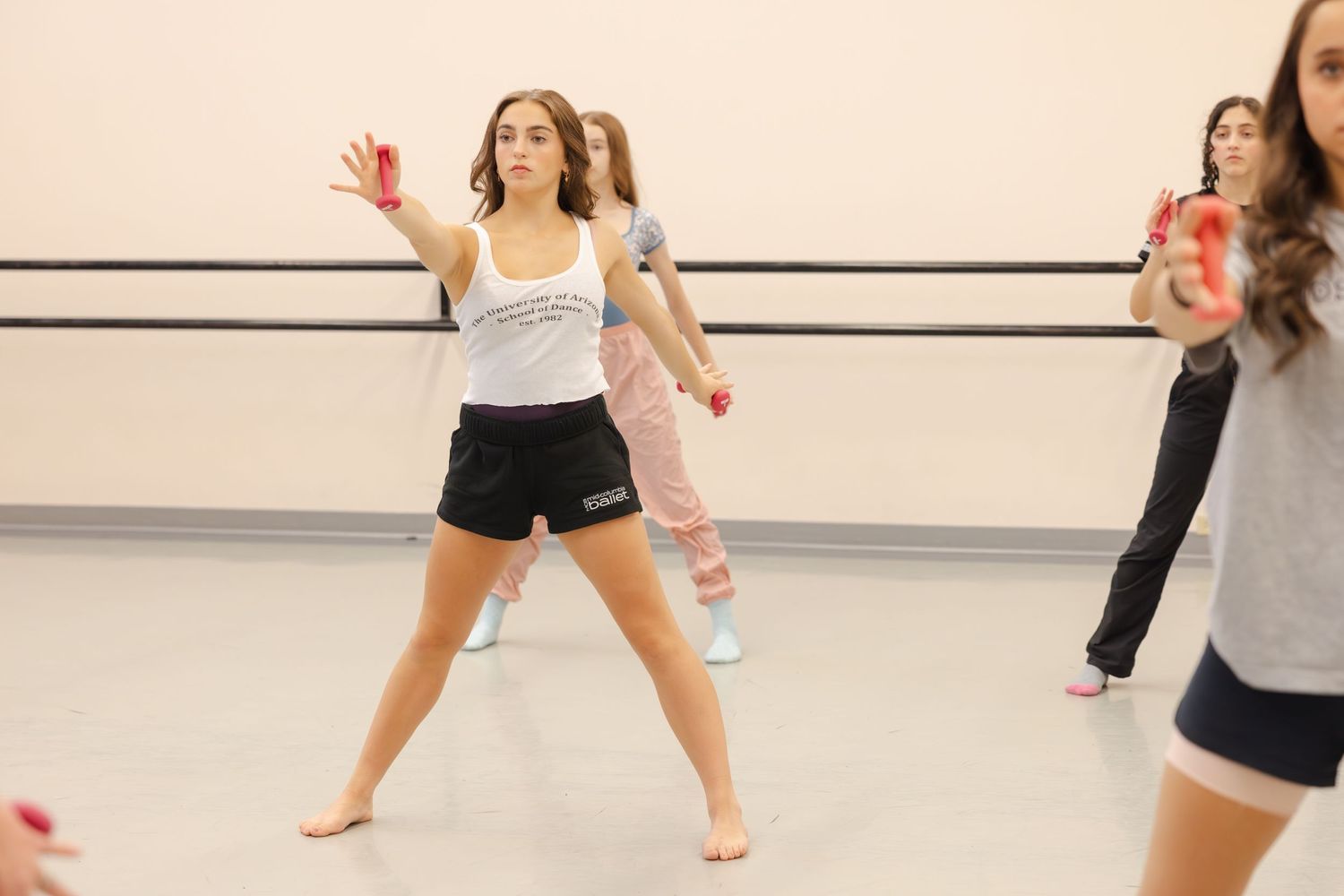 A dancer in black shorts and white tank top strikes a pose during dance practice in a studio.
