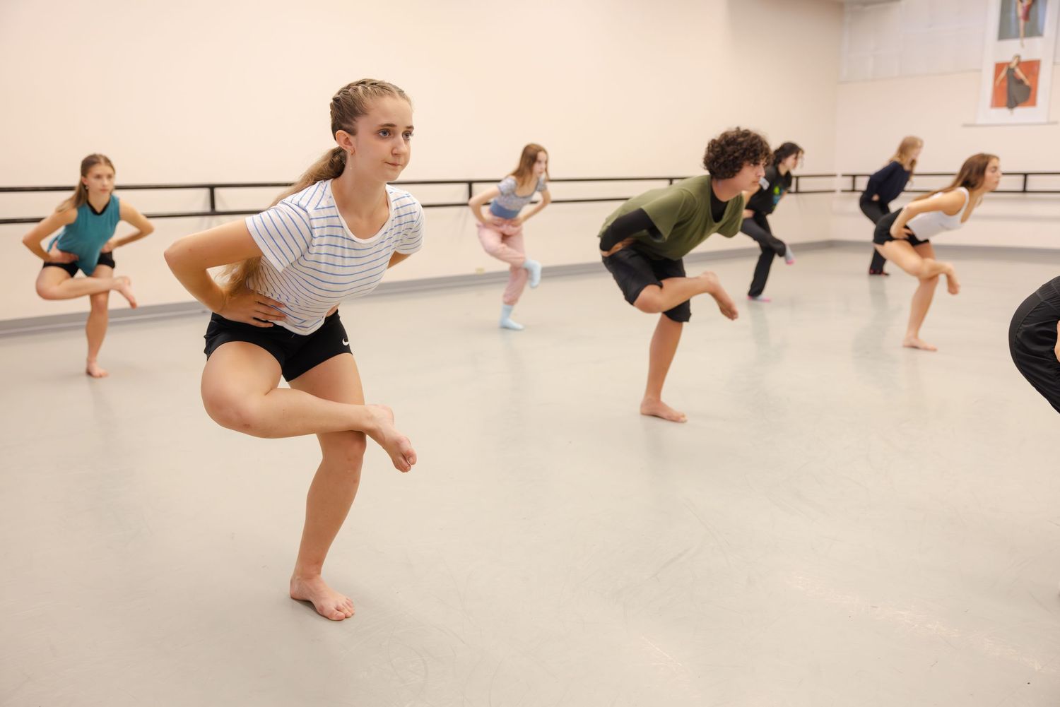 Dance students practice modern choreography in a bright studio with a ballet barre along the wall.