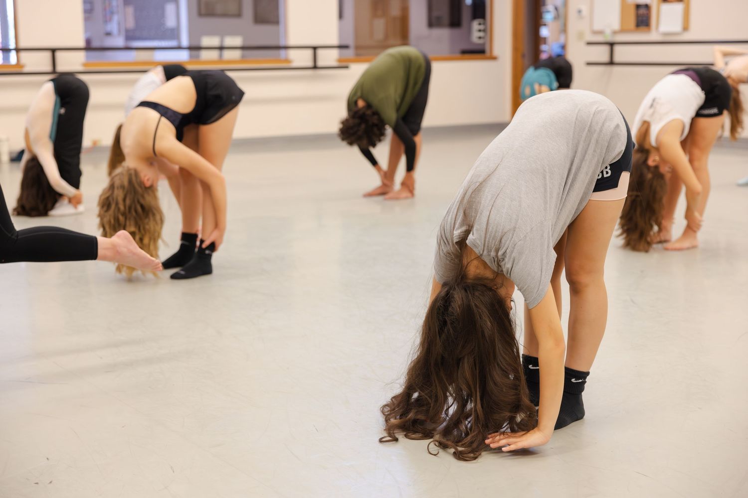 Dance students practicing forward bends in a mirrored studio during modern dance class.