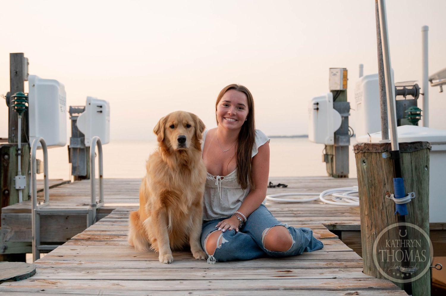 Golden Retriever and person sitting on marina dock during sunset.