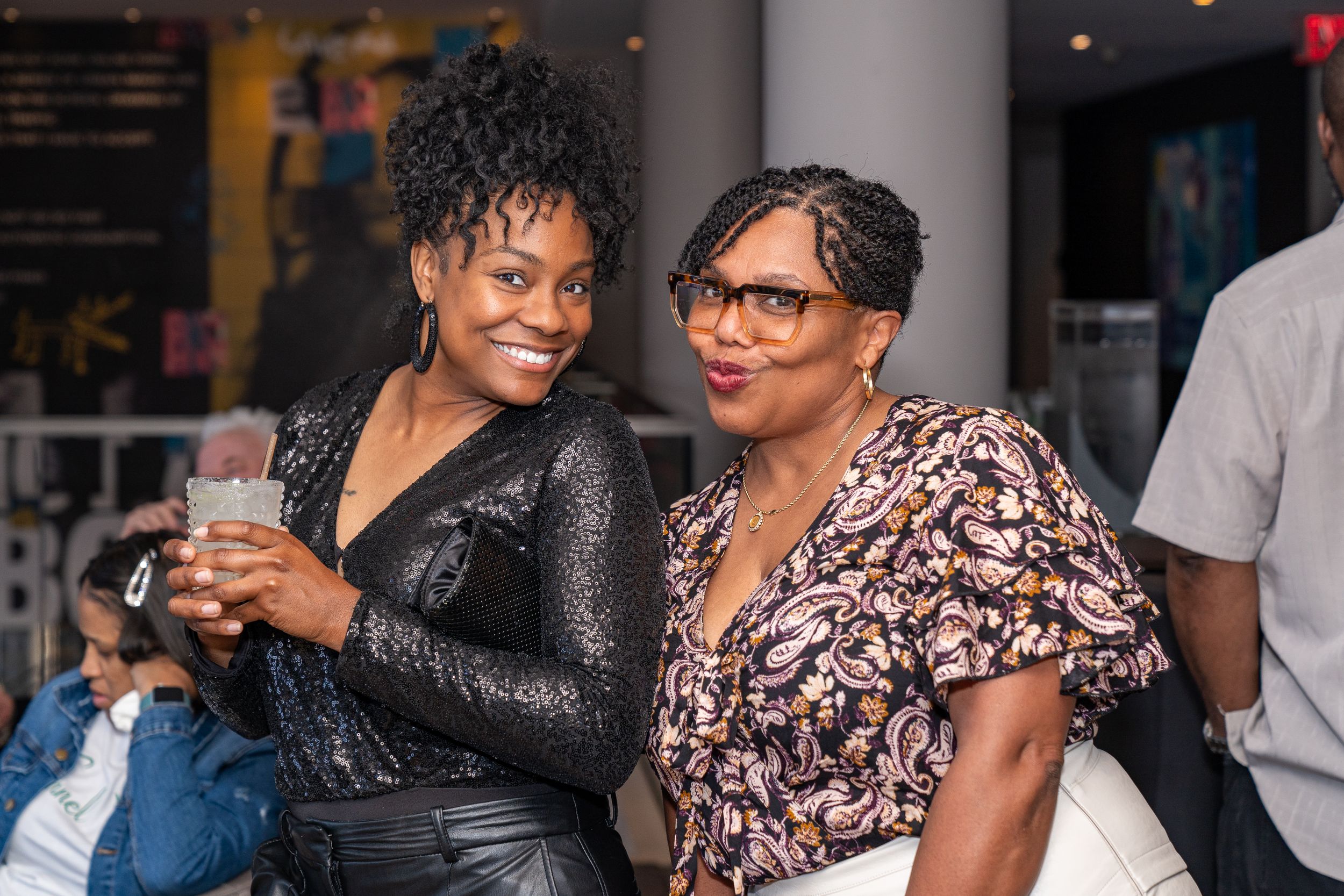 Two friends enjoying themselves at a social gathering wearing a sparkly black top and floral print dress.