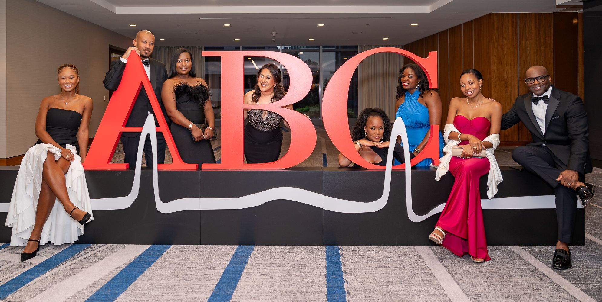 Group photo of elegantly dressed attendees posing in front of large ABC logo wall display.