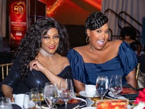 Formal dinner guests in evening attire enjoying conversation at elegant table setting.