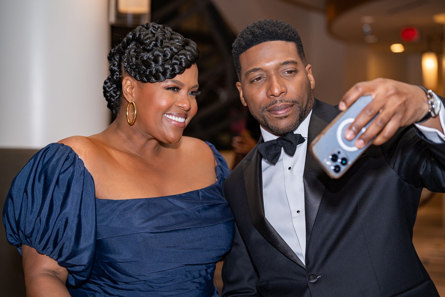 Elegant couple in formal attire pose together at an evening event, with the woman in navy and man in tuxedo.