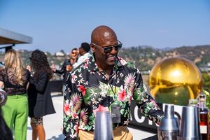 A person in a floral shirt and sunglasses enjoys an outdoor event with a golden sphere decoration.