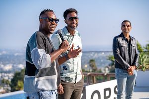 Three people engaged in conversation at an outdoor rooftop gathering with city views.