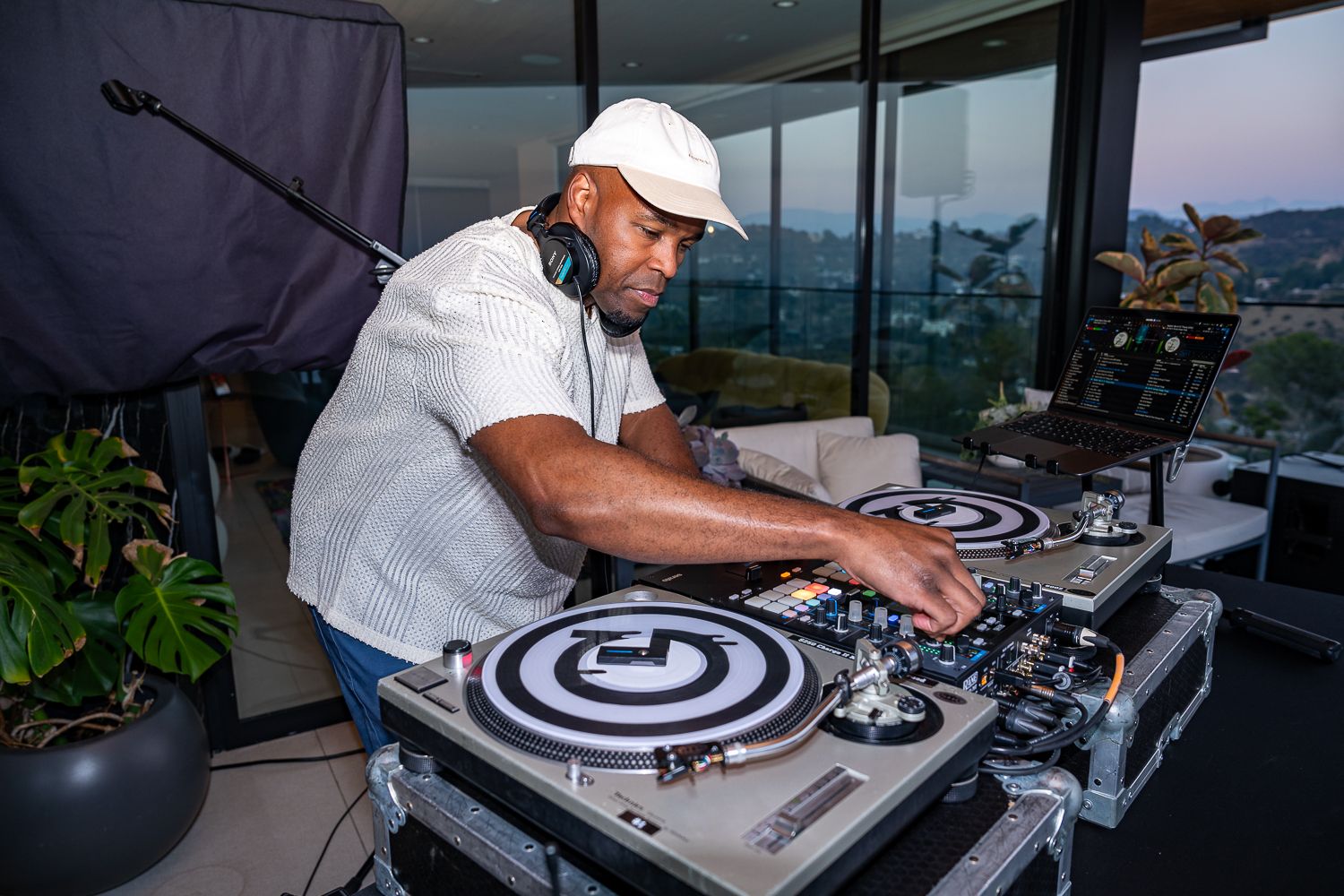 DJ performs on turntables at an outdoor event wearing white cap and shirt.