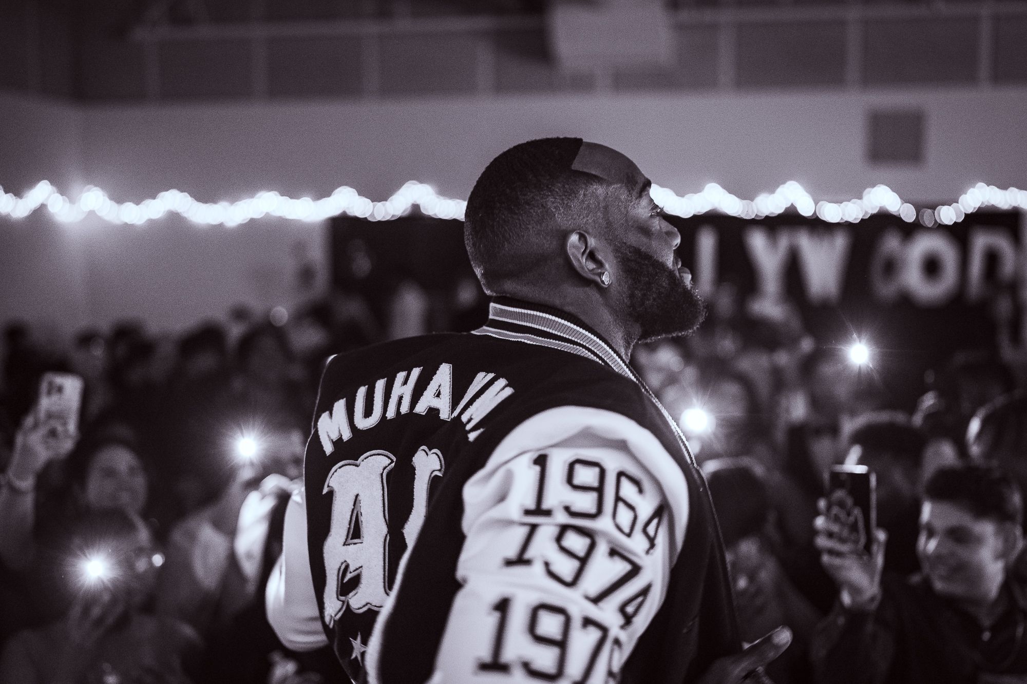 Black and white photo of performer wearing varsity jacket at crowded event.