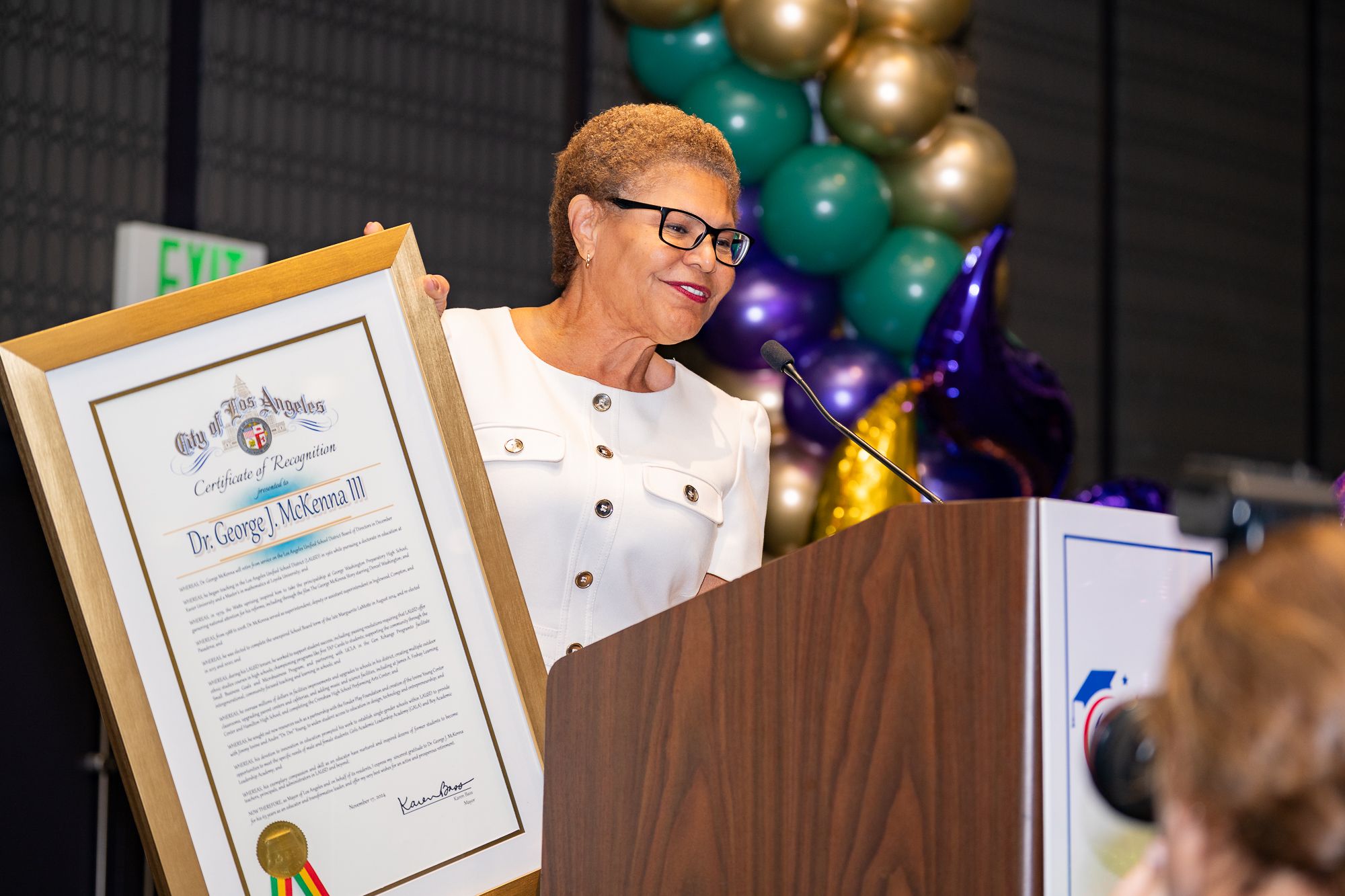 Person holding award certificate at podium with festive balloon decorations.