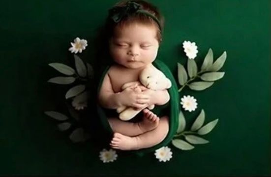 Newborn photography setup with green backdrop and delicate white flowers.